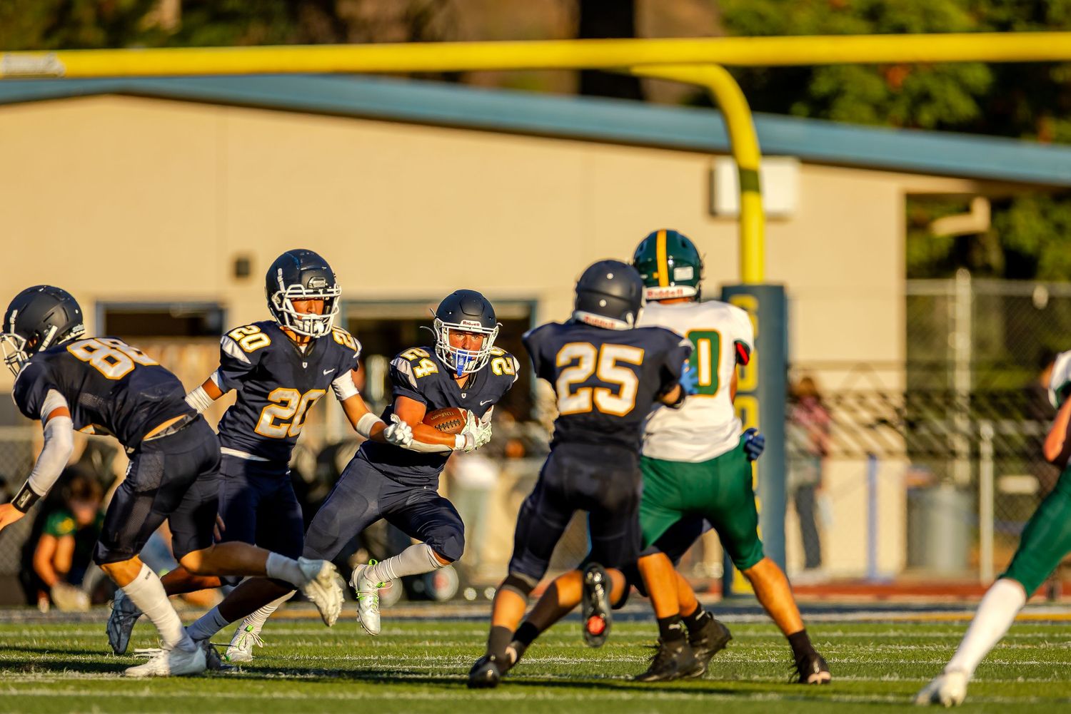 Athletes line up on a football field during a game with bright sunlight casting shadows on the turf.