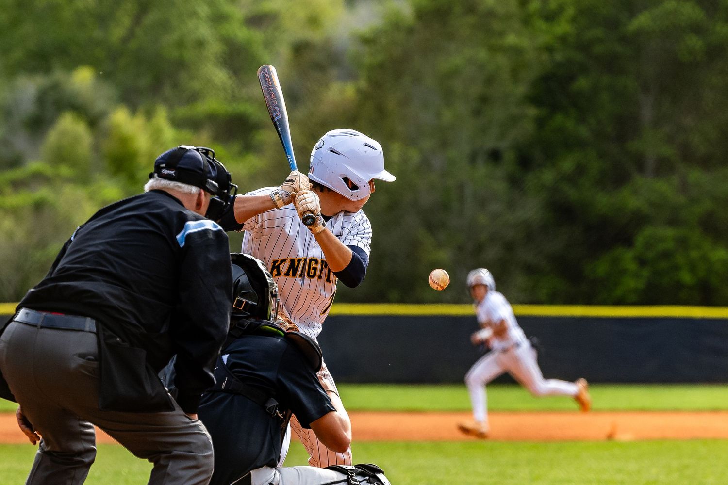 Baseball players in dark uniforms prepare for action on a sunny baseball diamond.