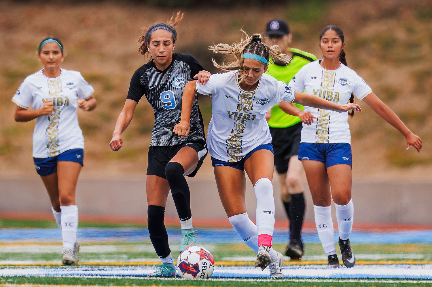 Soccer players sprint and compete for the ball during an intense match on a sunny field.