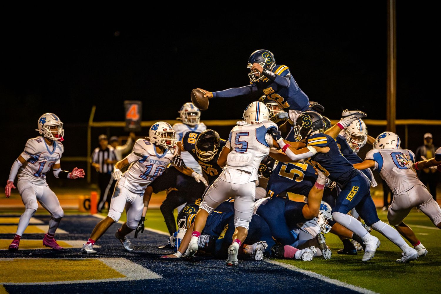 Football players engaged in an intense line of scrimmage play during a nighttime game.