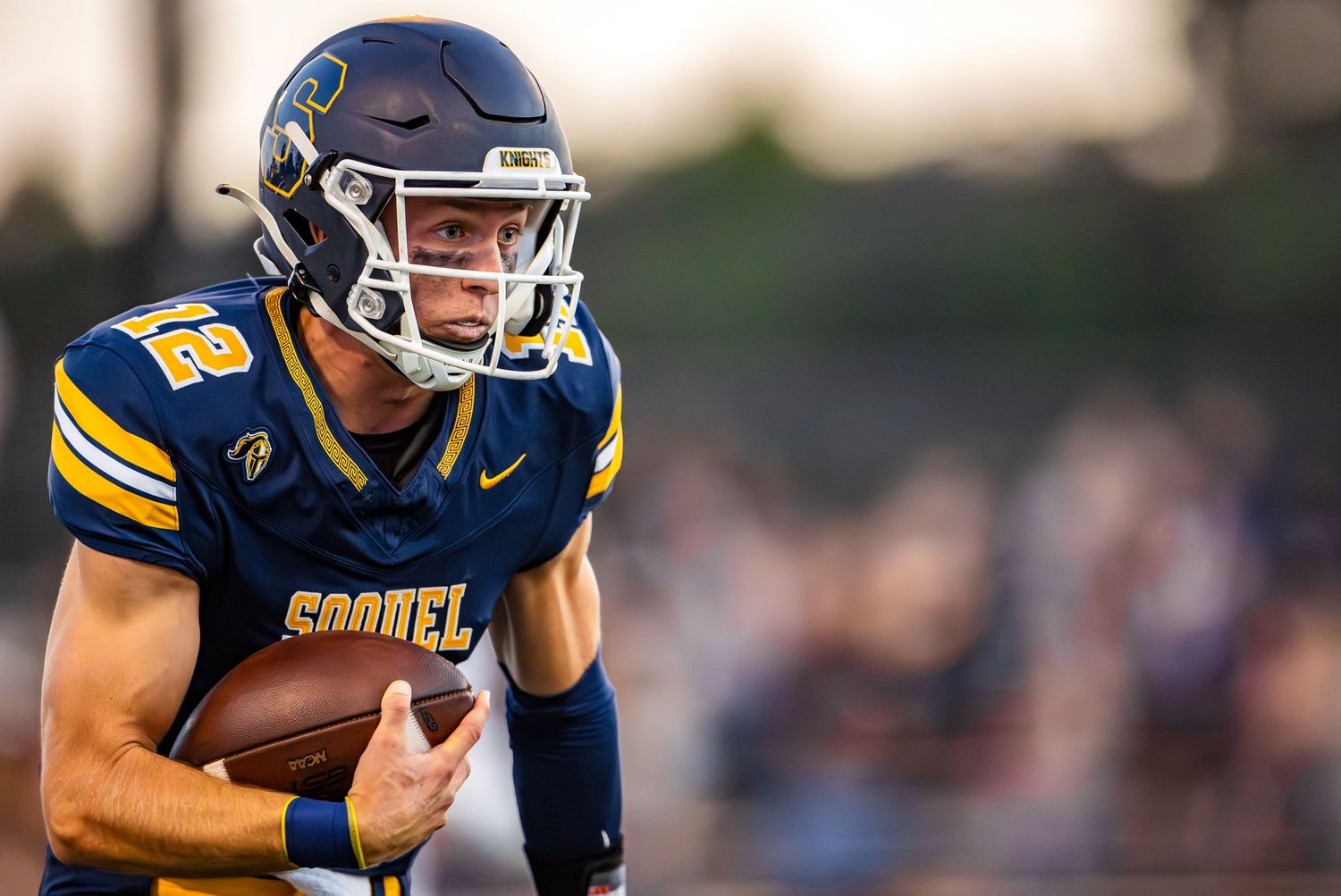 Football player in yellow and blue uniform runs with the ball during a game at outdoor stadium.