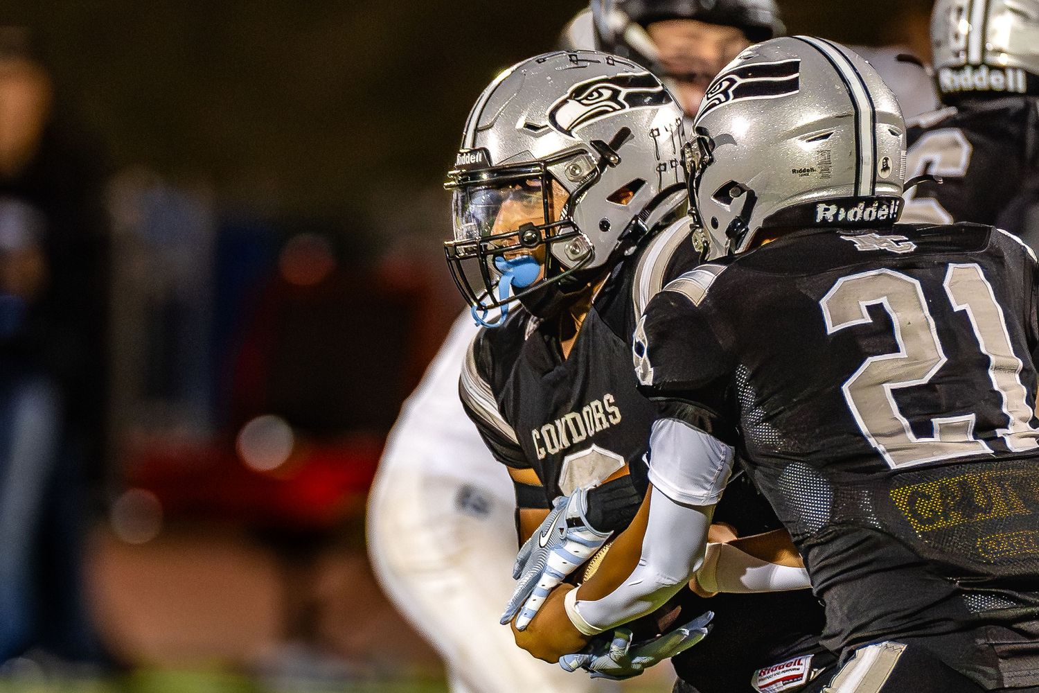 Football players in black and white uniforms battle for control during a nighttime game.