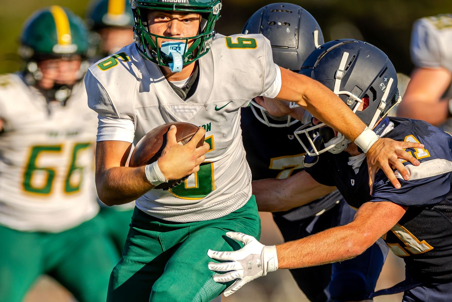 Football players in green and white uniforms collide during an intense game action sequence.