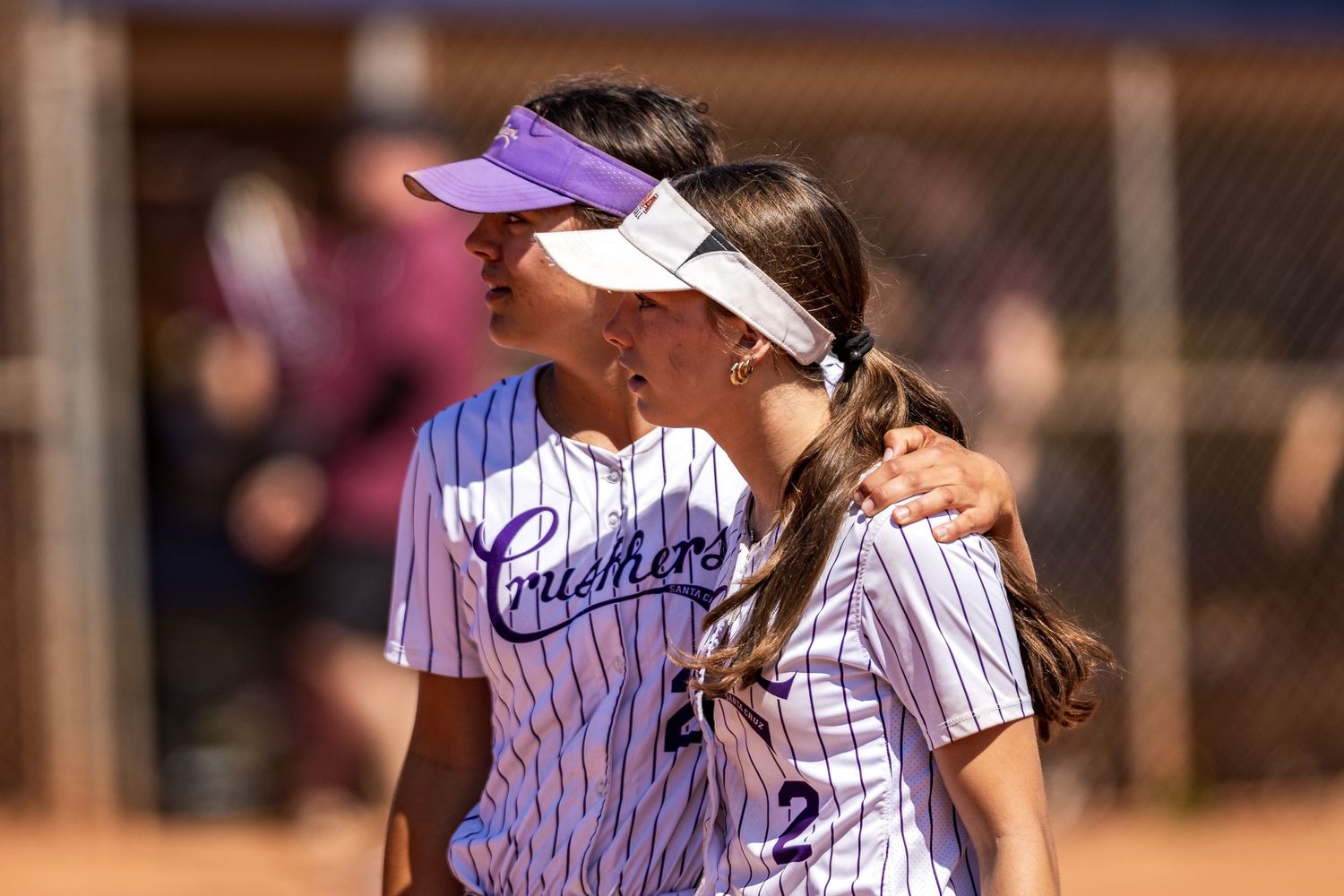 Softball player wearing a purple visor and white pinstriped uniform smiles during a sunny game on the field.