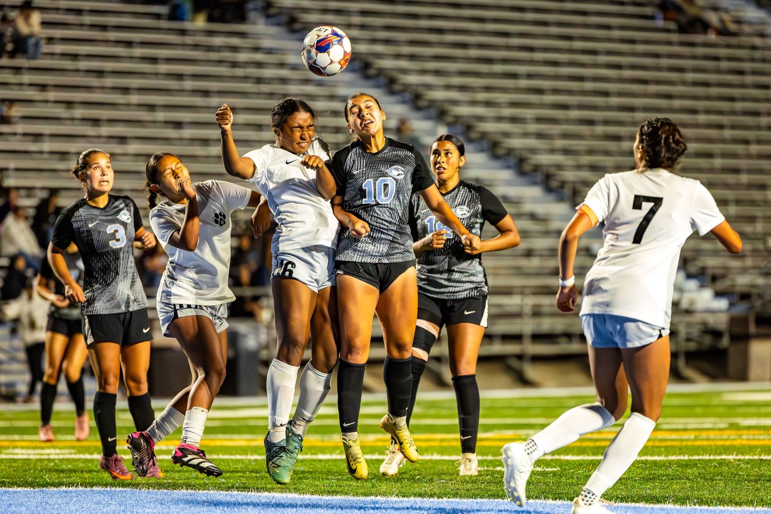 Soccer players compete for possession of the ball during an intense match on a floodlit field.