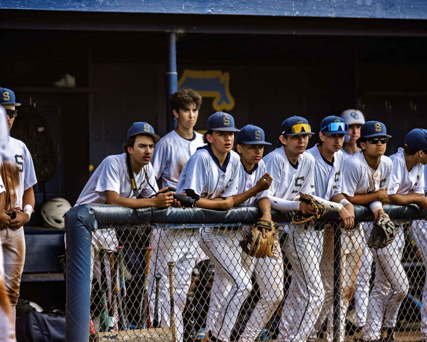 Baseball players and coaches line up along a dugout fence during a game at Fenway Park.