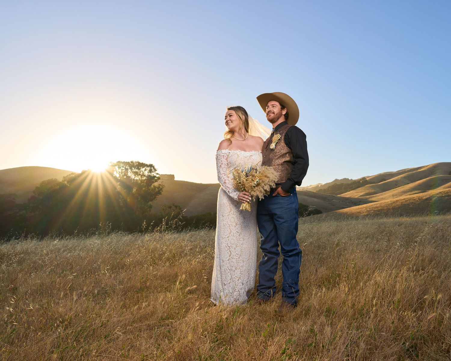 A couple staring proudly into the mountains with the sun behind them.