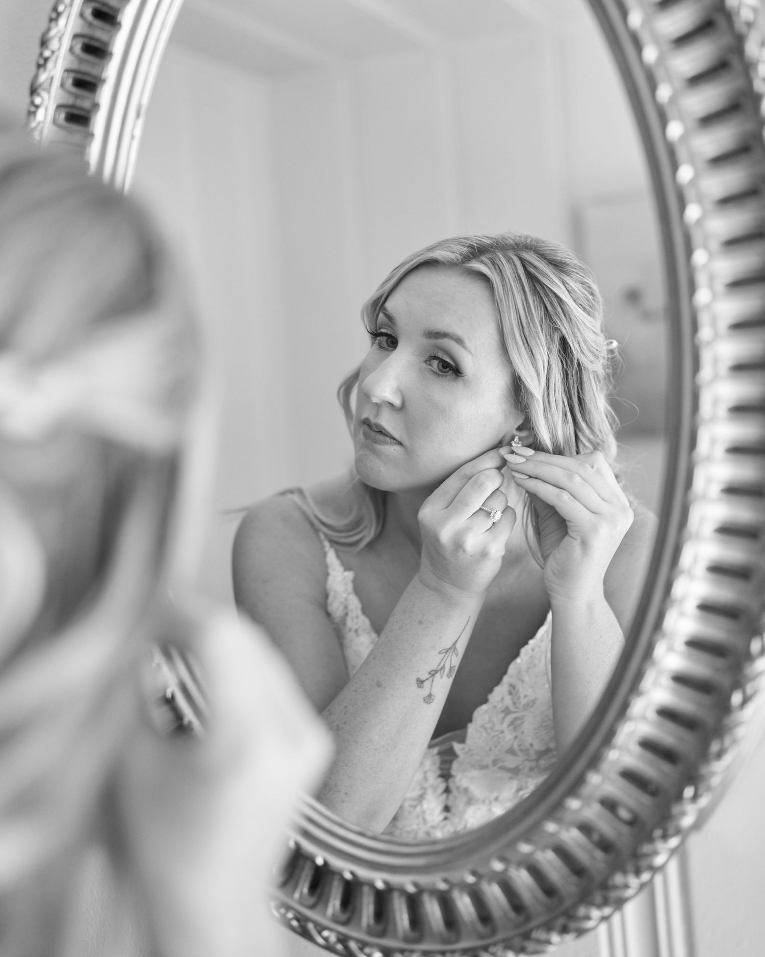 A bride putting on her earrings in the mirror.