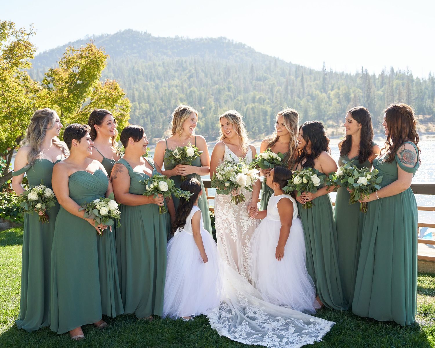 A bride and her bridesmaids smiling at each other during a bright day.