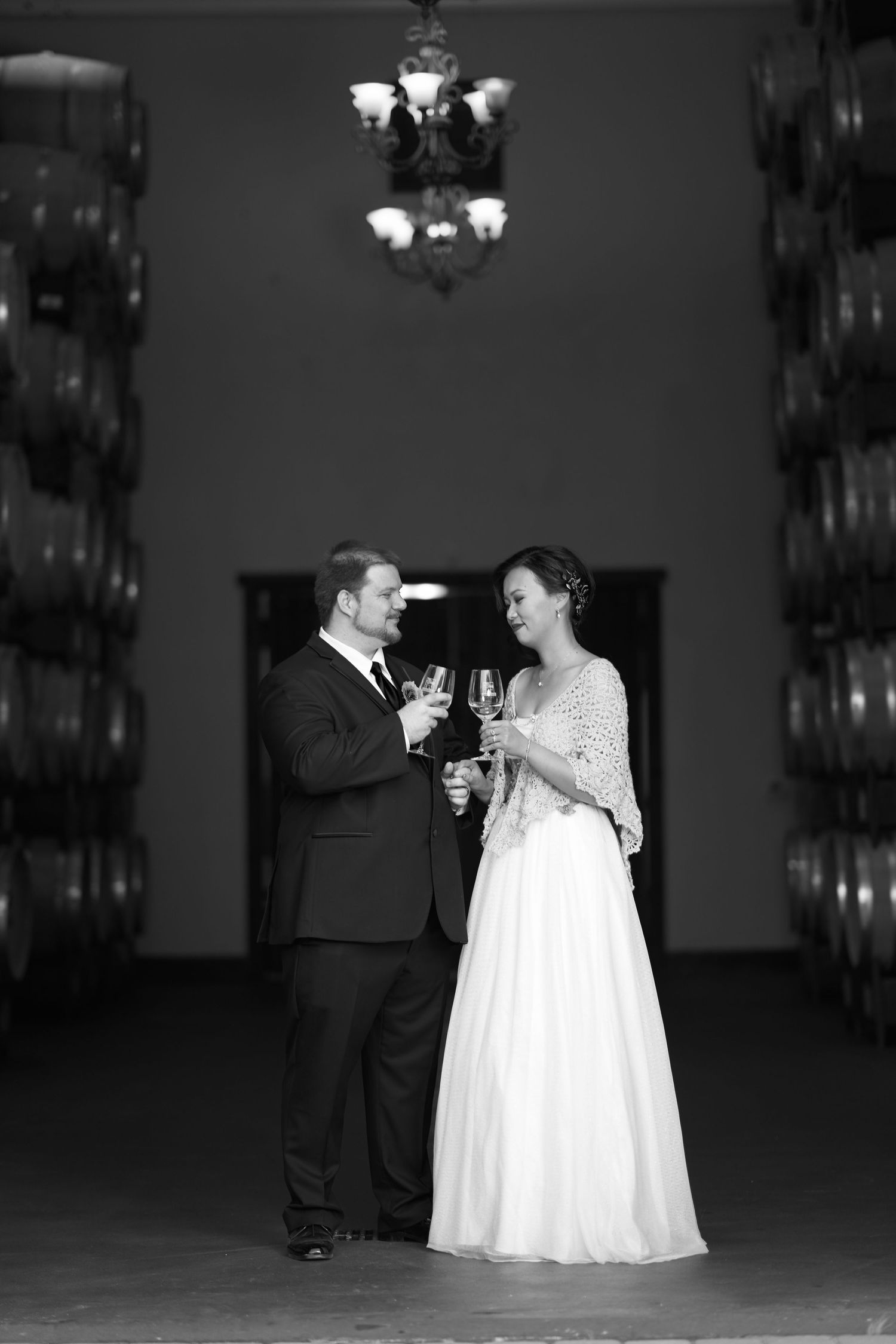 A couple holding wine glasses in front of a winery barrel room.