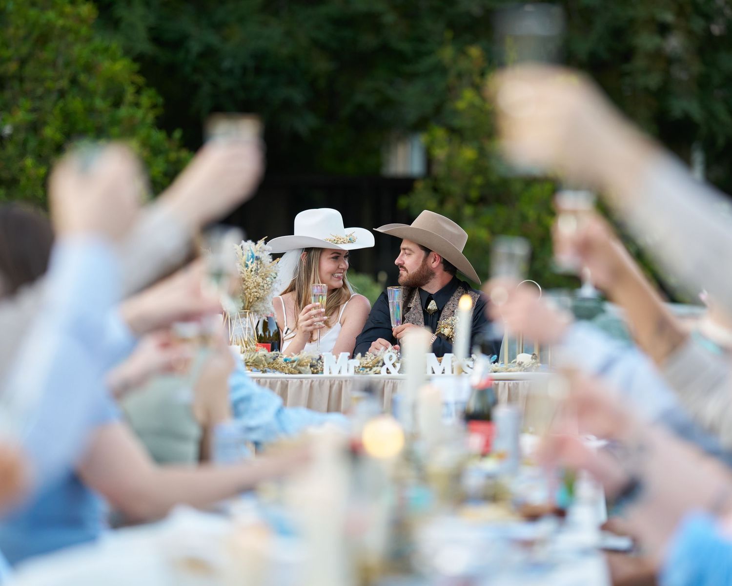 A couple toasting to each other with their friends and family also toasting in the foreground.
