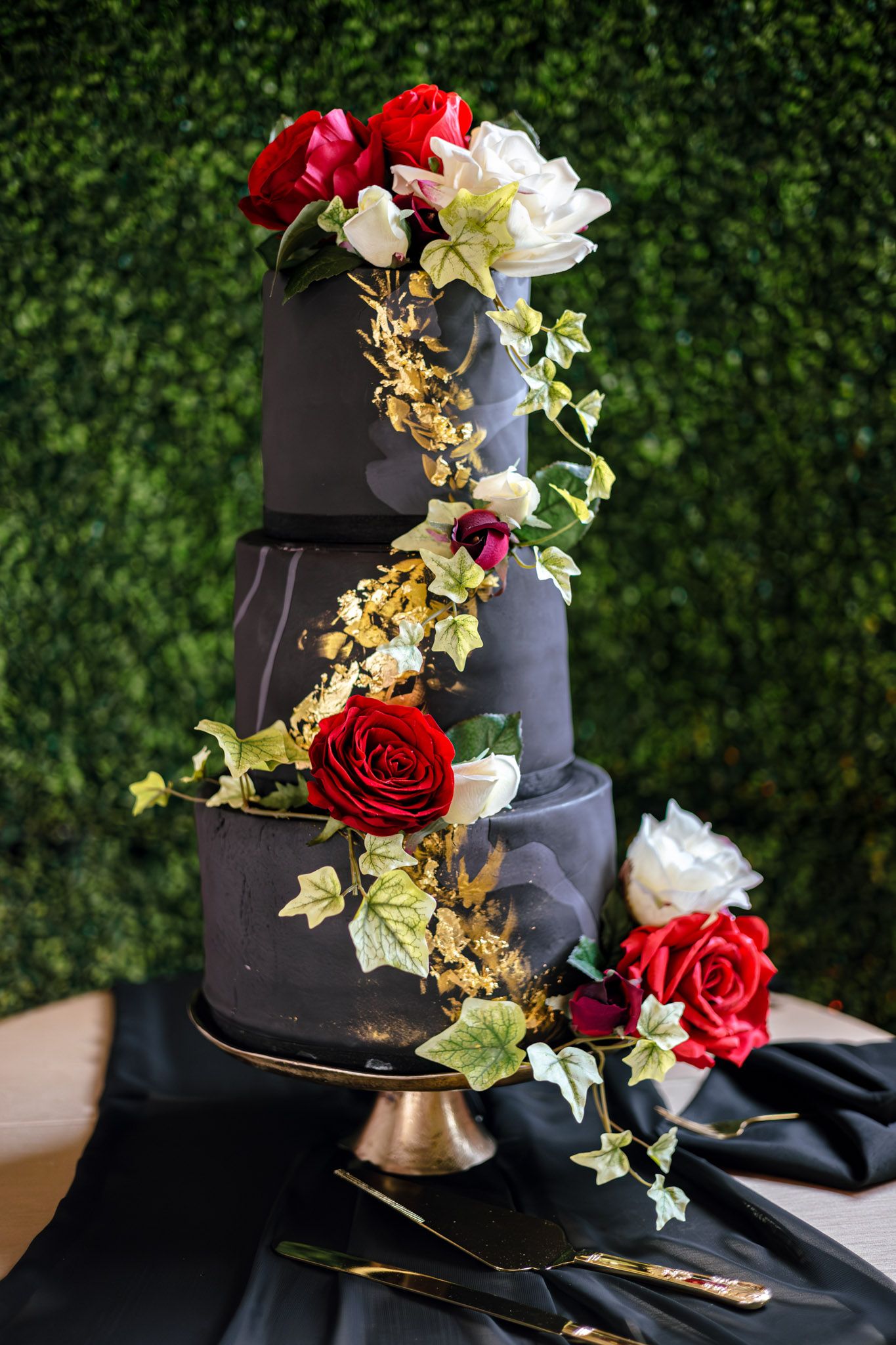 black 3-tier wedding cake with gold accents and red roses