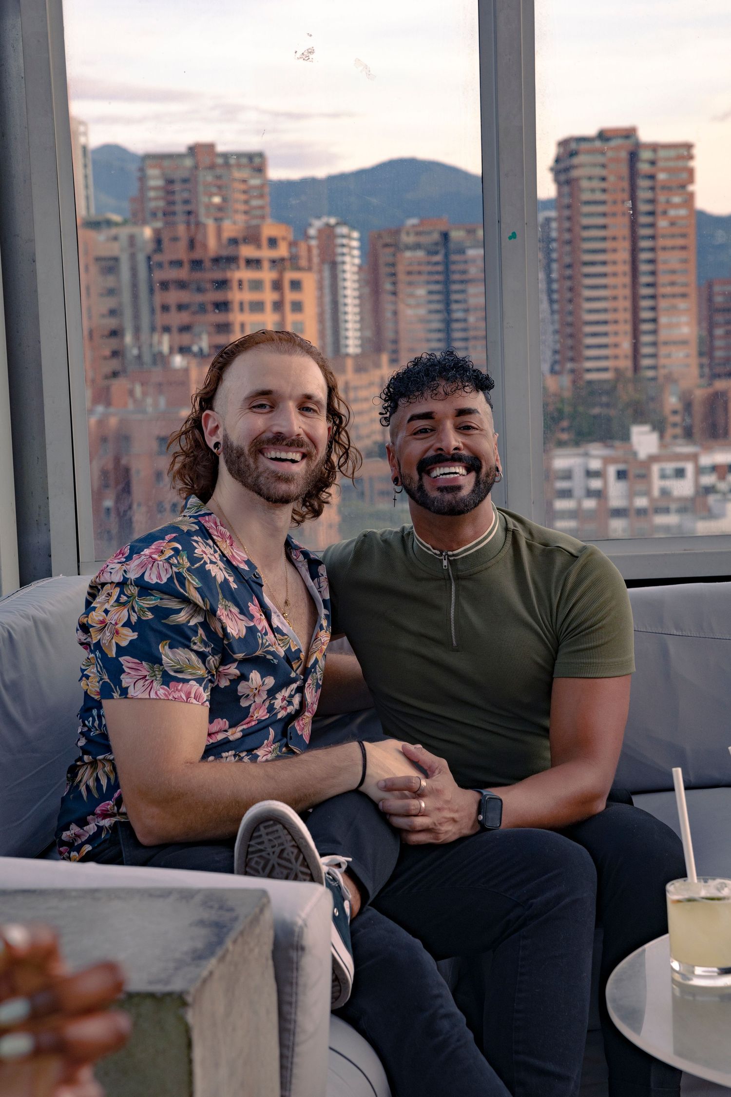 A couple portrait posing on a cozy couch enjoying a rooftop view of a city skyline with high-rise buildings at sunset