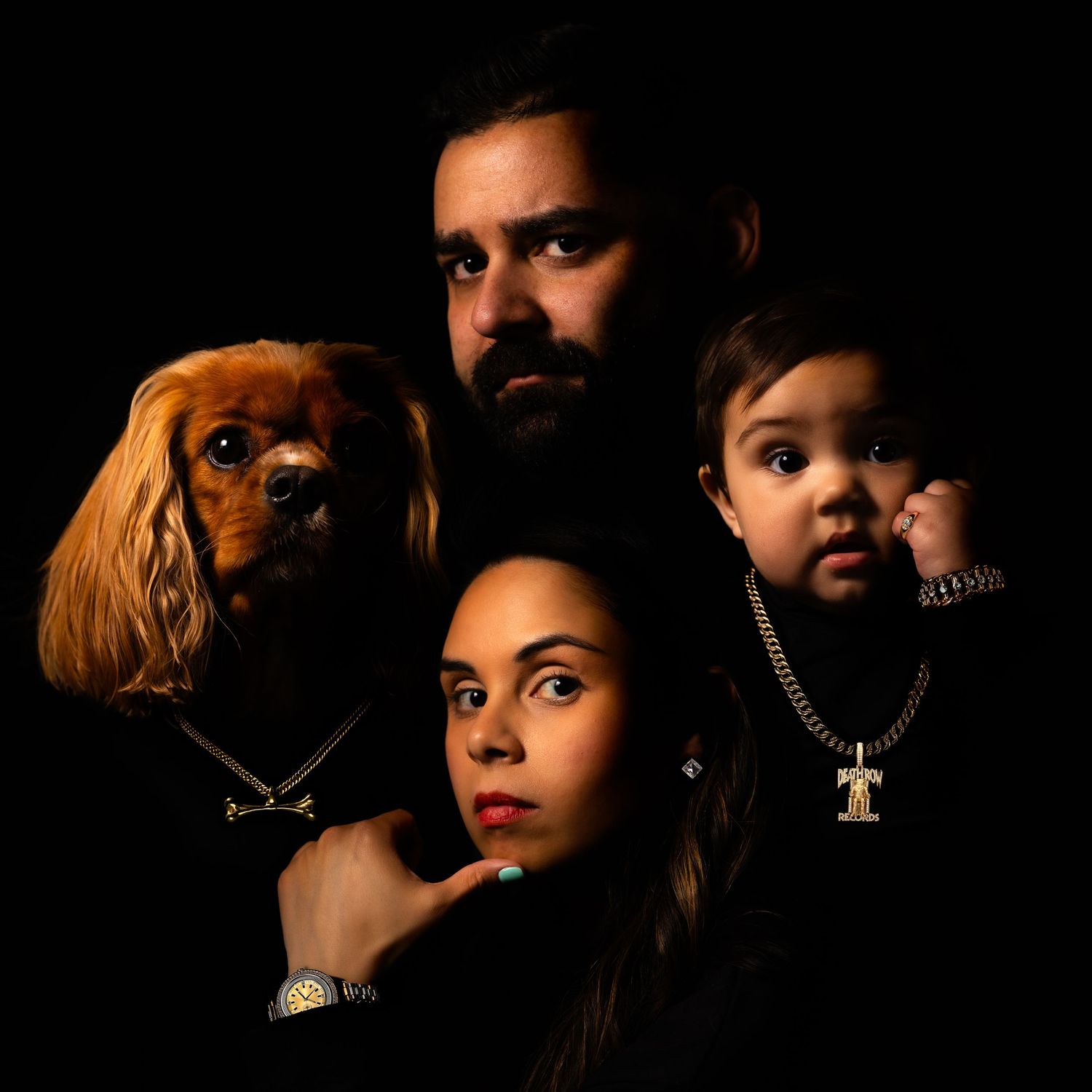 Dark dramatic portrait of a family and their brown Cavalier King Charles Spaniel dog against black background,recreating Death Row Records