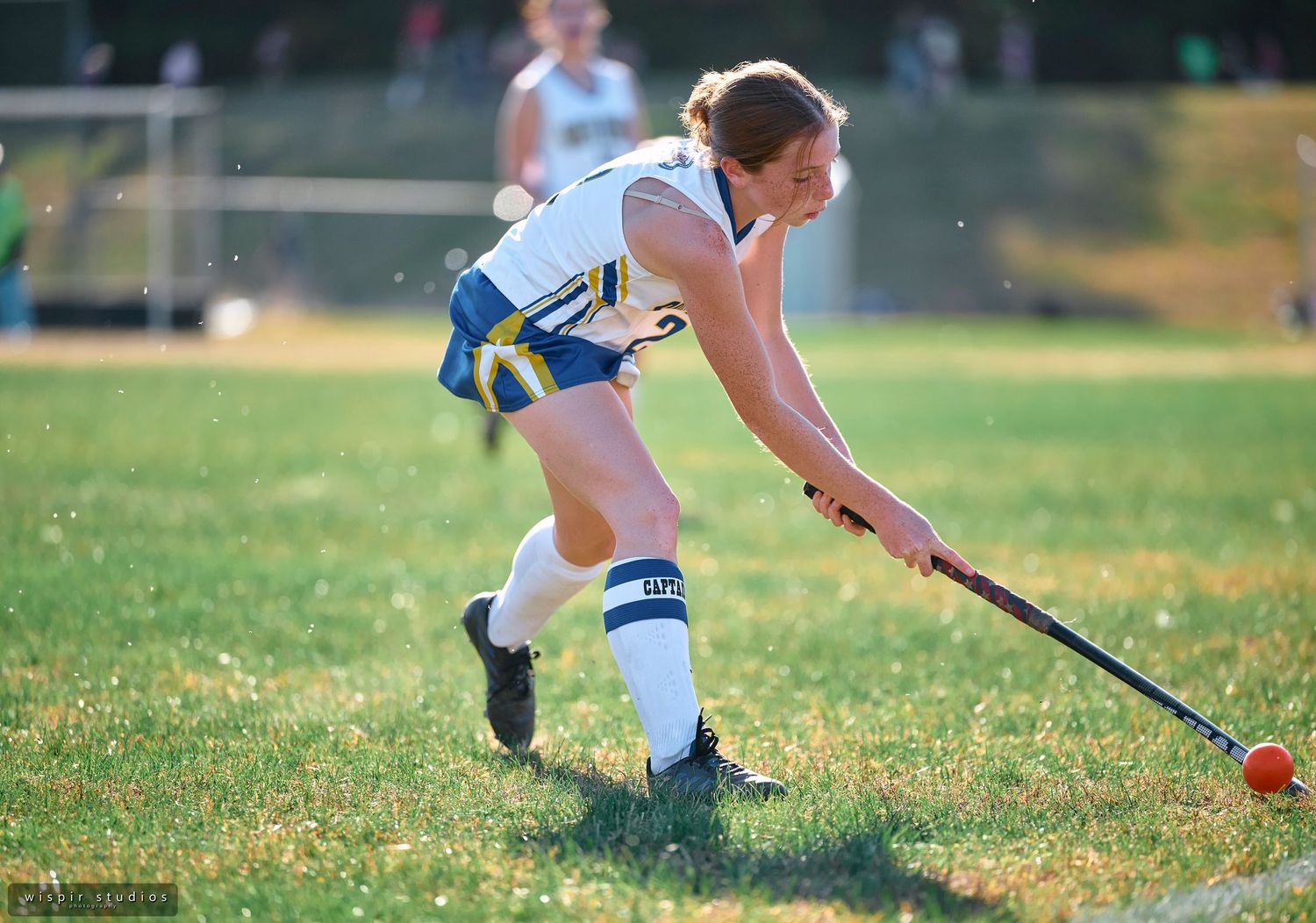 Field hockey players compete for control of the ball during an intense match on a sunny grass field.