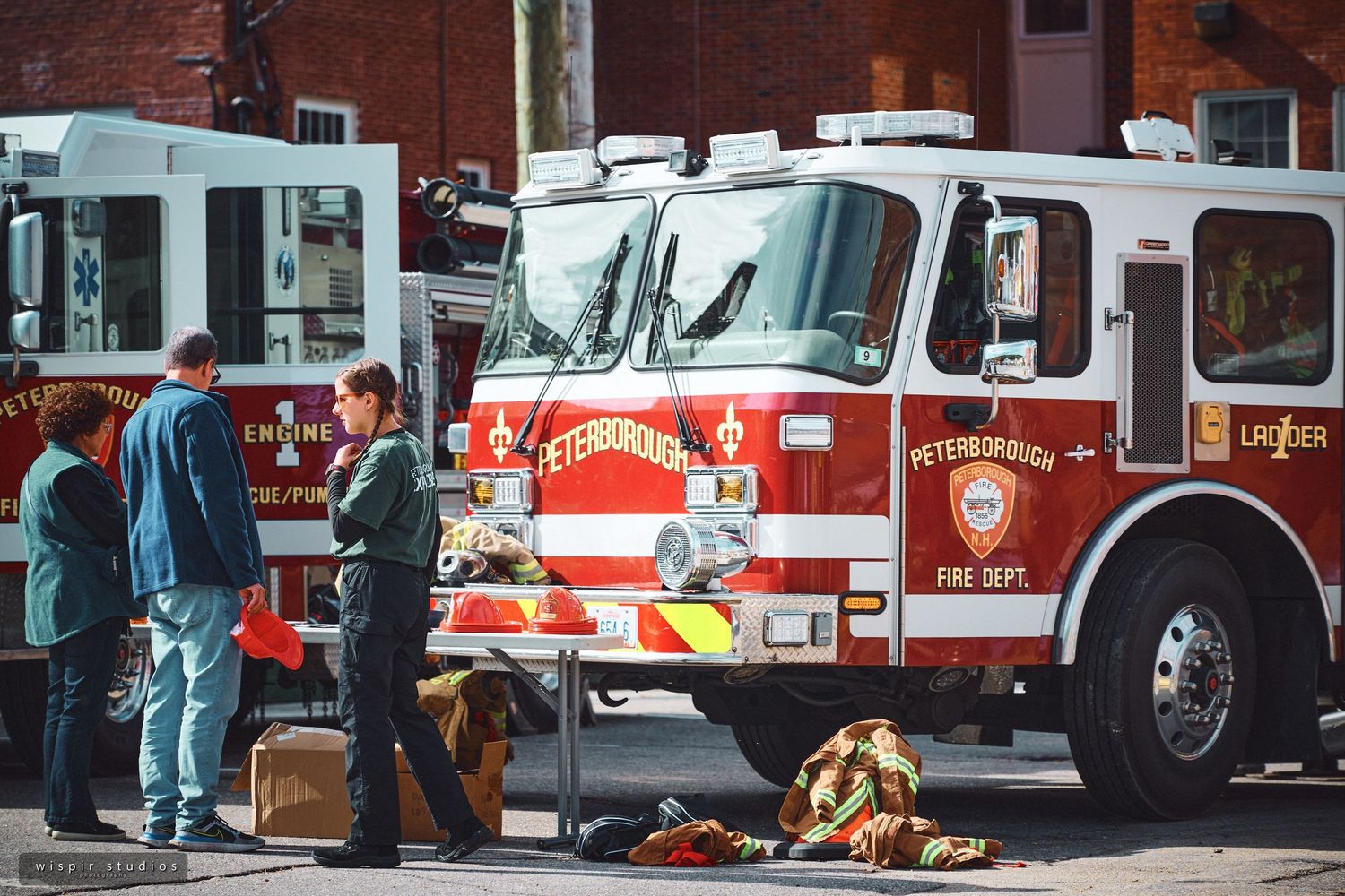 Row of red and white fire trucks and emergency vehicles parked outside a brick building.