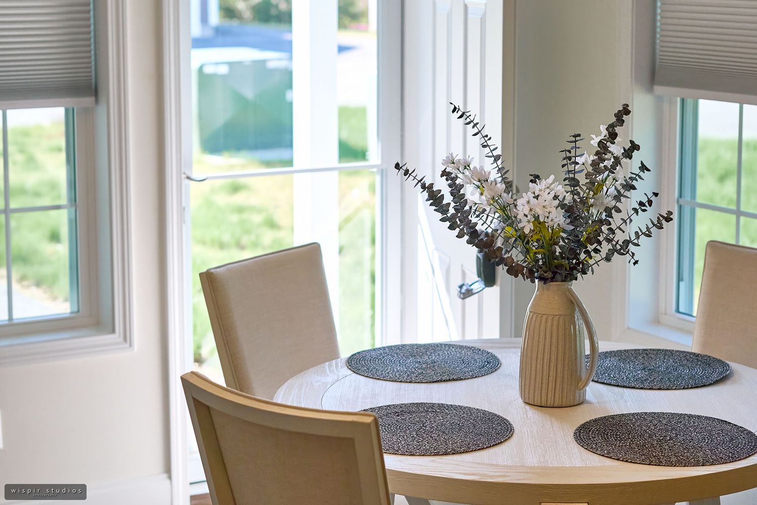 A row of identical gray and white vases with dried flowers sit on a windowsill in natural light.