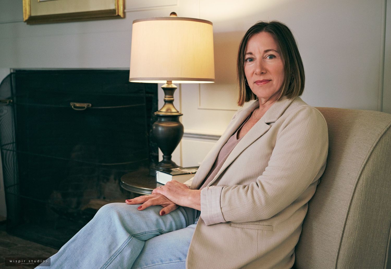 A person in a beige blazer sits on a couch in a modern living room setting with warm lighting.