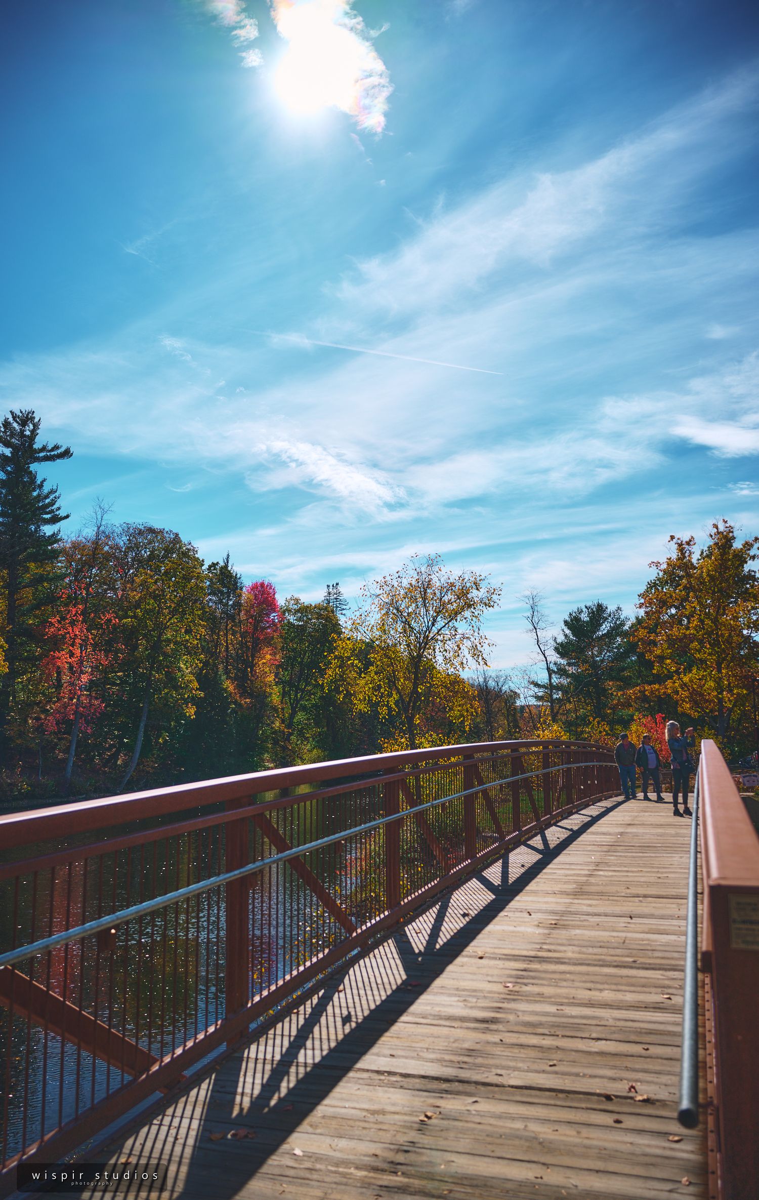 Wooden boardwalk extends through colorful fall foliage under bright blue skies.