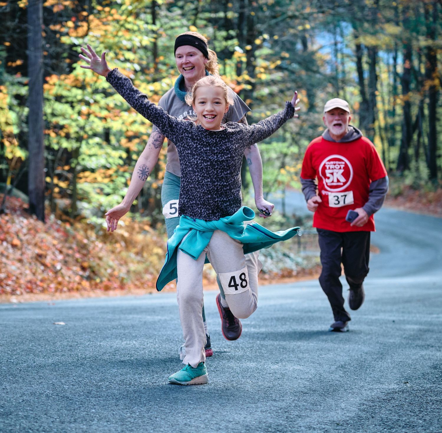 Runners leap playfully on an autumn road during a fun outdoor fitness event.