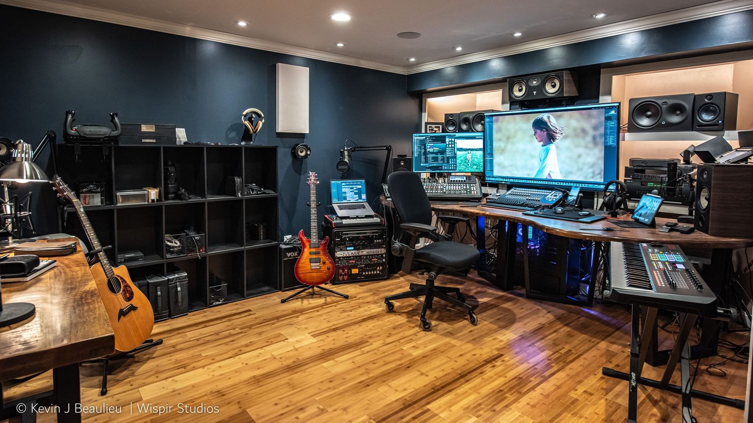 Professional music recording studio with guitars, mixing console, dual monitors, acoustic panels, and hardwood floors.