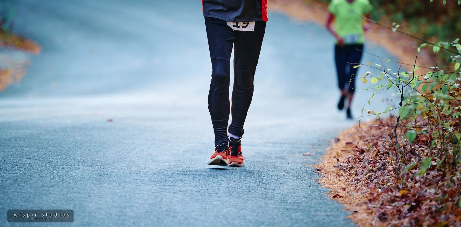 Athletes running on a scenic forest path with fall foliage in the background.