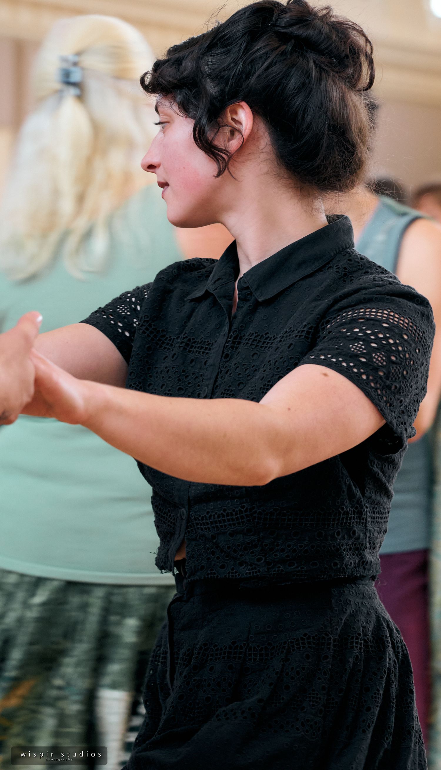 A dancer in black lace performs graceful movements in profile against a light background.