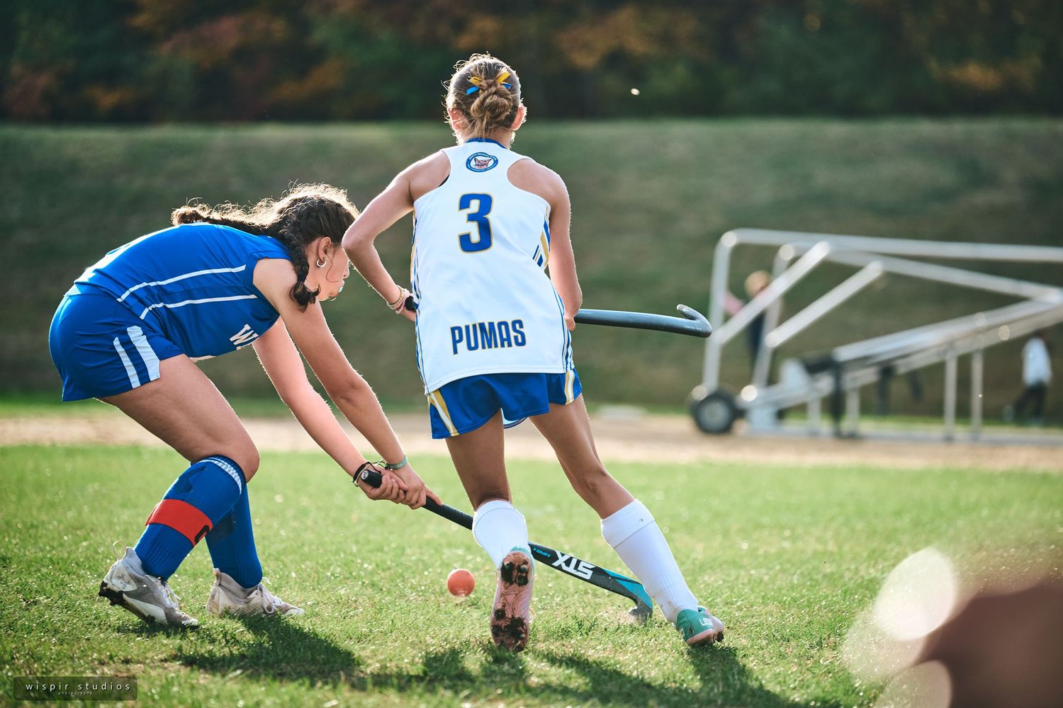 Soccer players in blue and white uniforms compete for possession of the ball during an outdoor match.