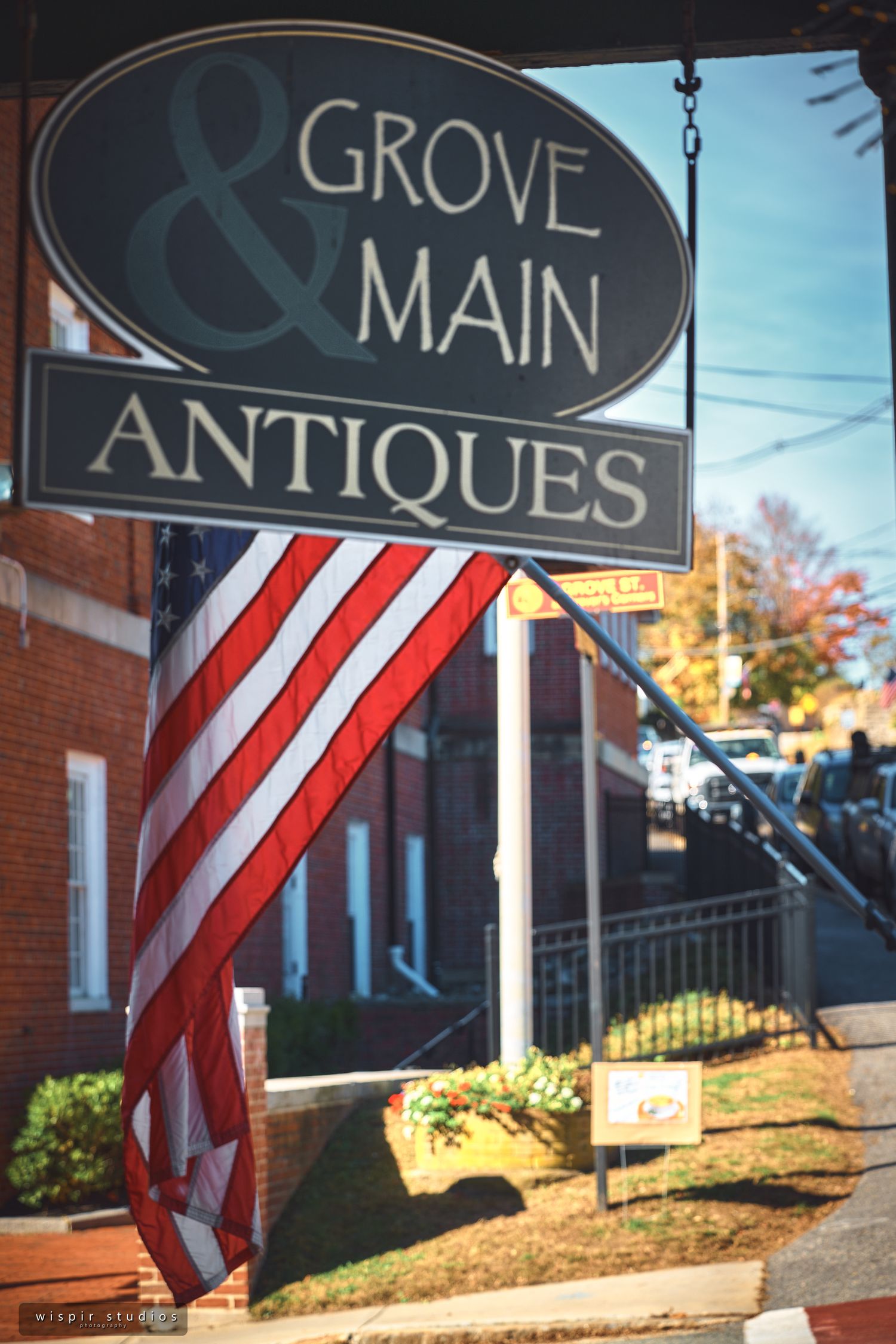 A vintage-style antique shop sign hangs with an American flag in the foreground.