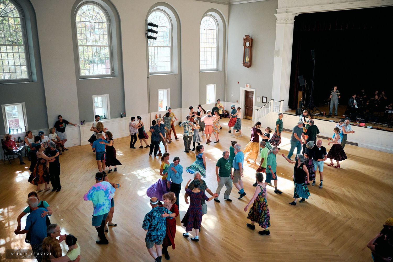 Large indoor space with arched windows and hardwood floors filled with event attendees.