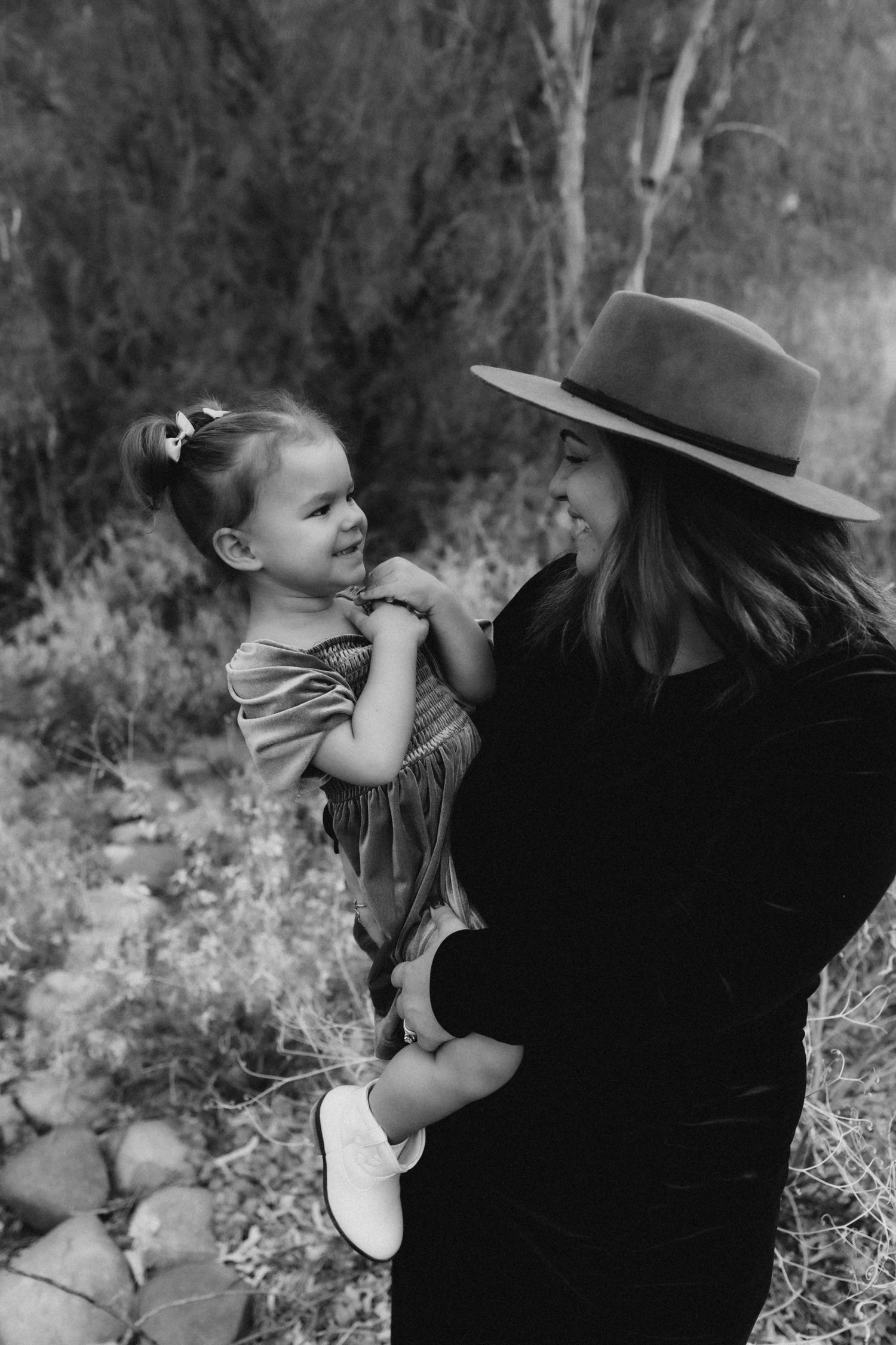 Black and white portrait of parent and child sharing a playful moment outdoors.