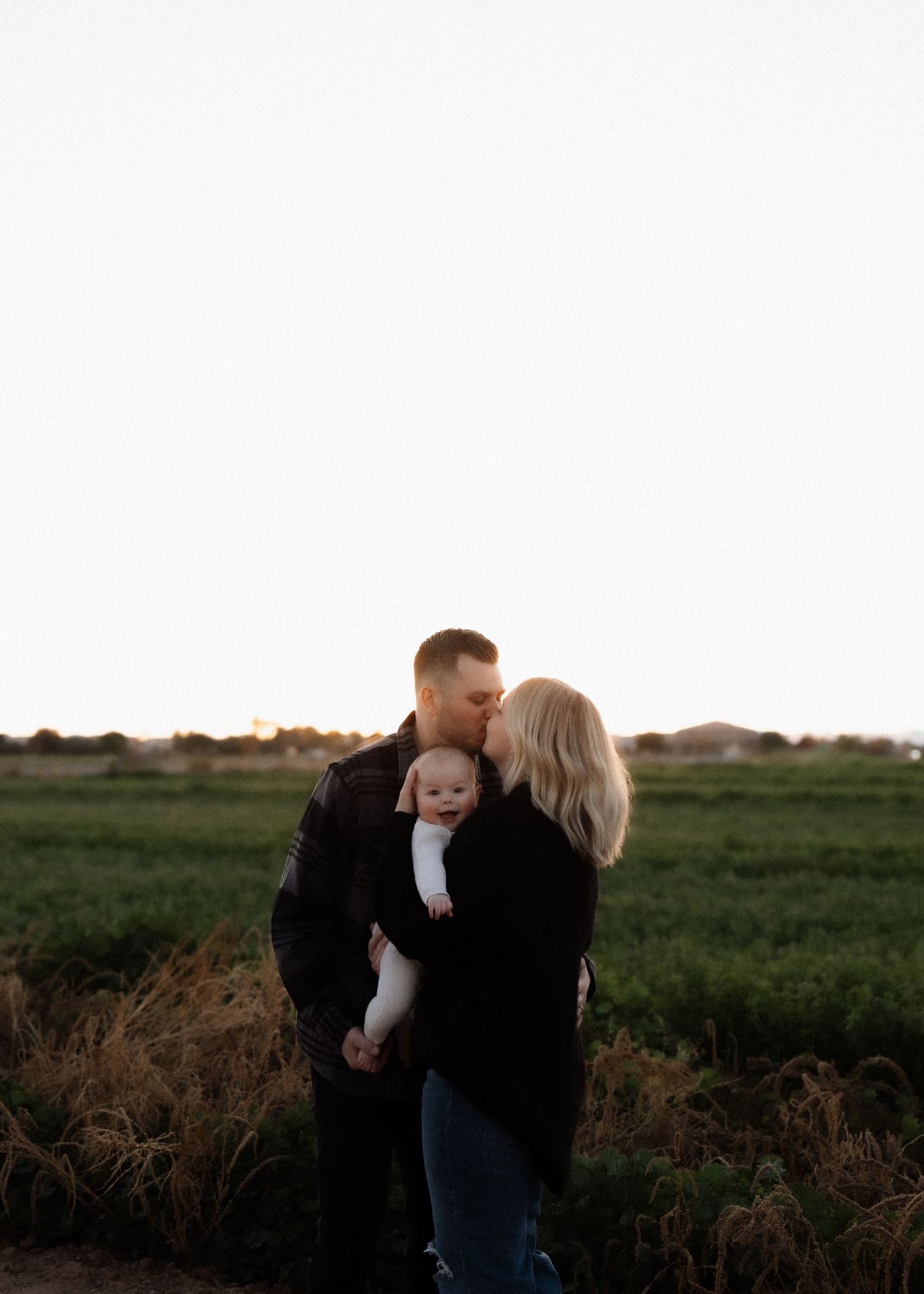 A family shares an intimate moment together in an outdoor field at sunset.