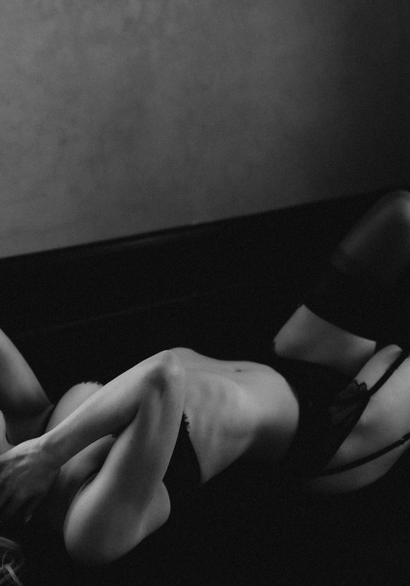 Black and white artistic boudoir photo showing shadows and curves in intimate lighting against dark background.