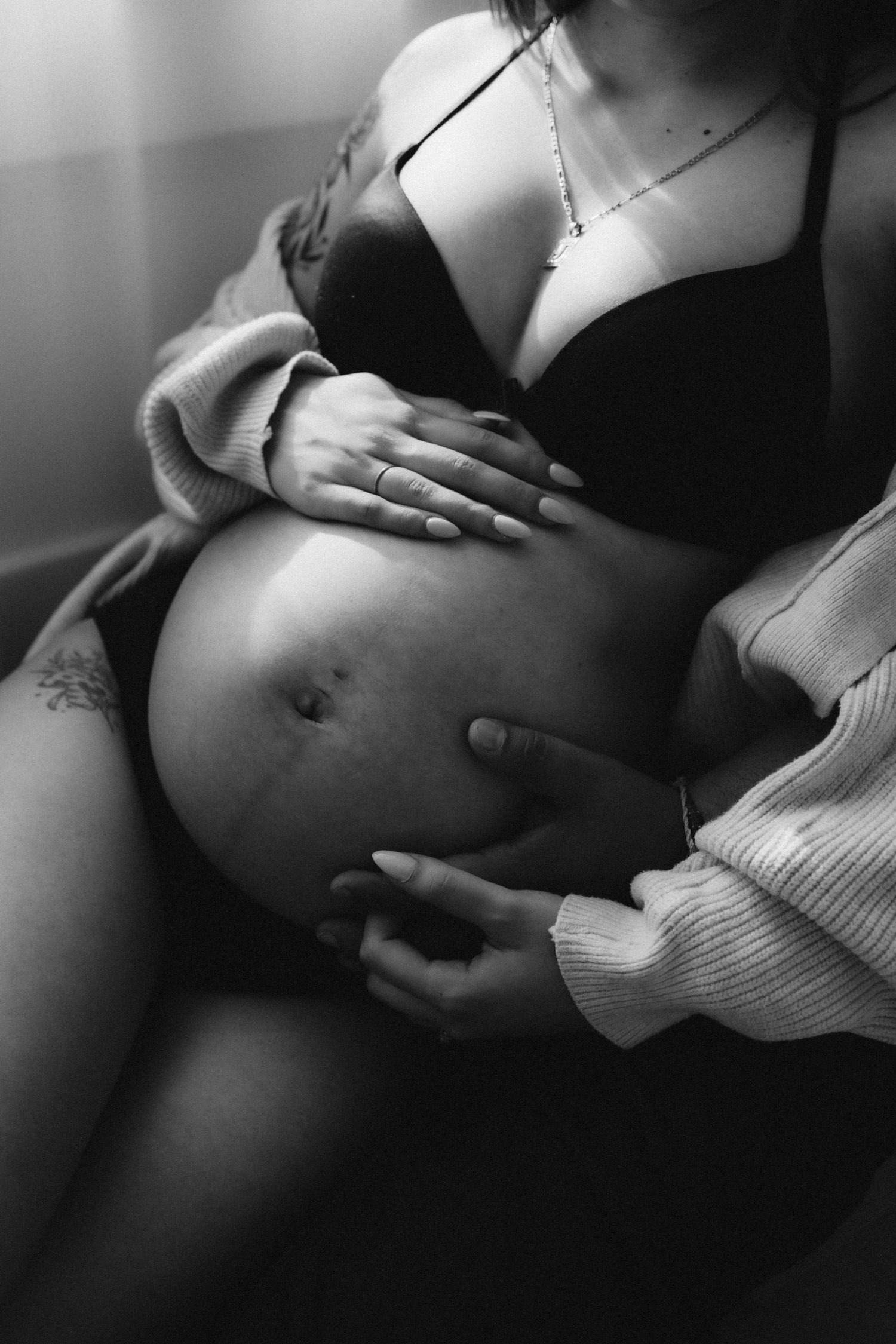 Artistic black and white maternity photo showing a pregnant belly with hands gently resting on it.