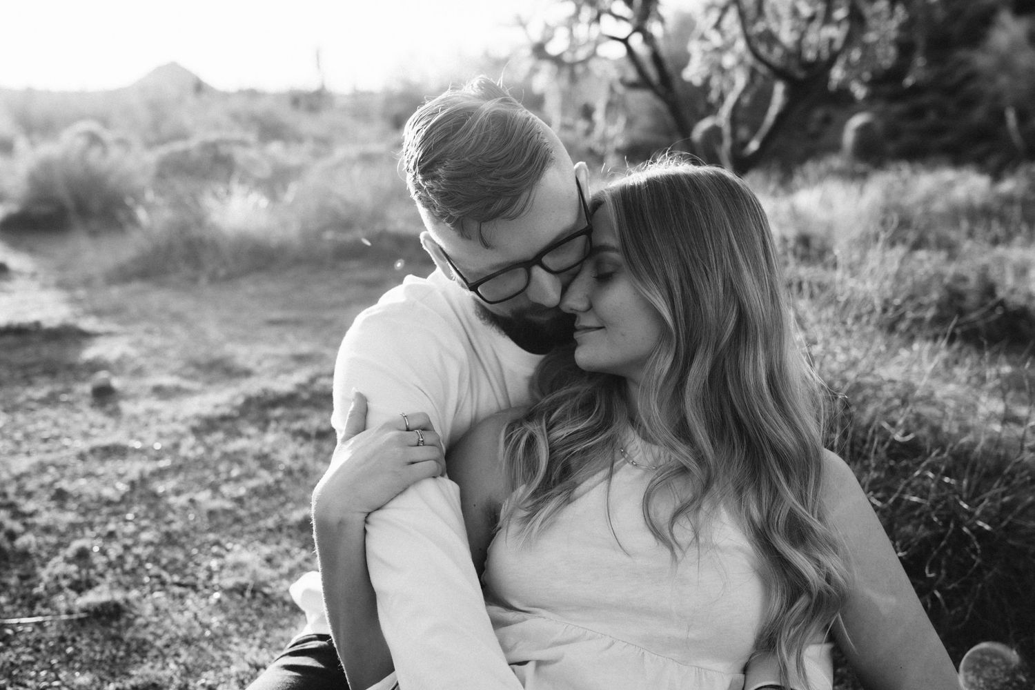 An intimate black and white portrait of a couple sharing a tender moment in the desert landscape.