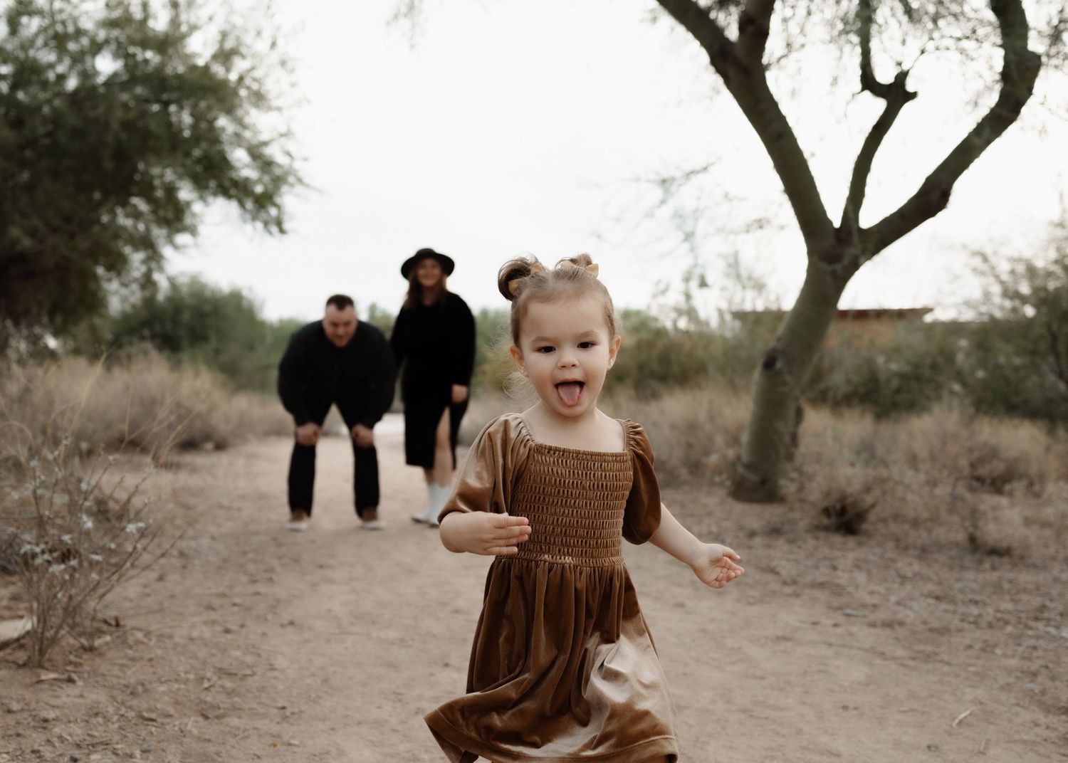 Child in brown dress runs along desert path while adults walk in background.