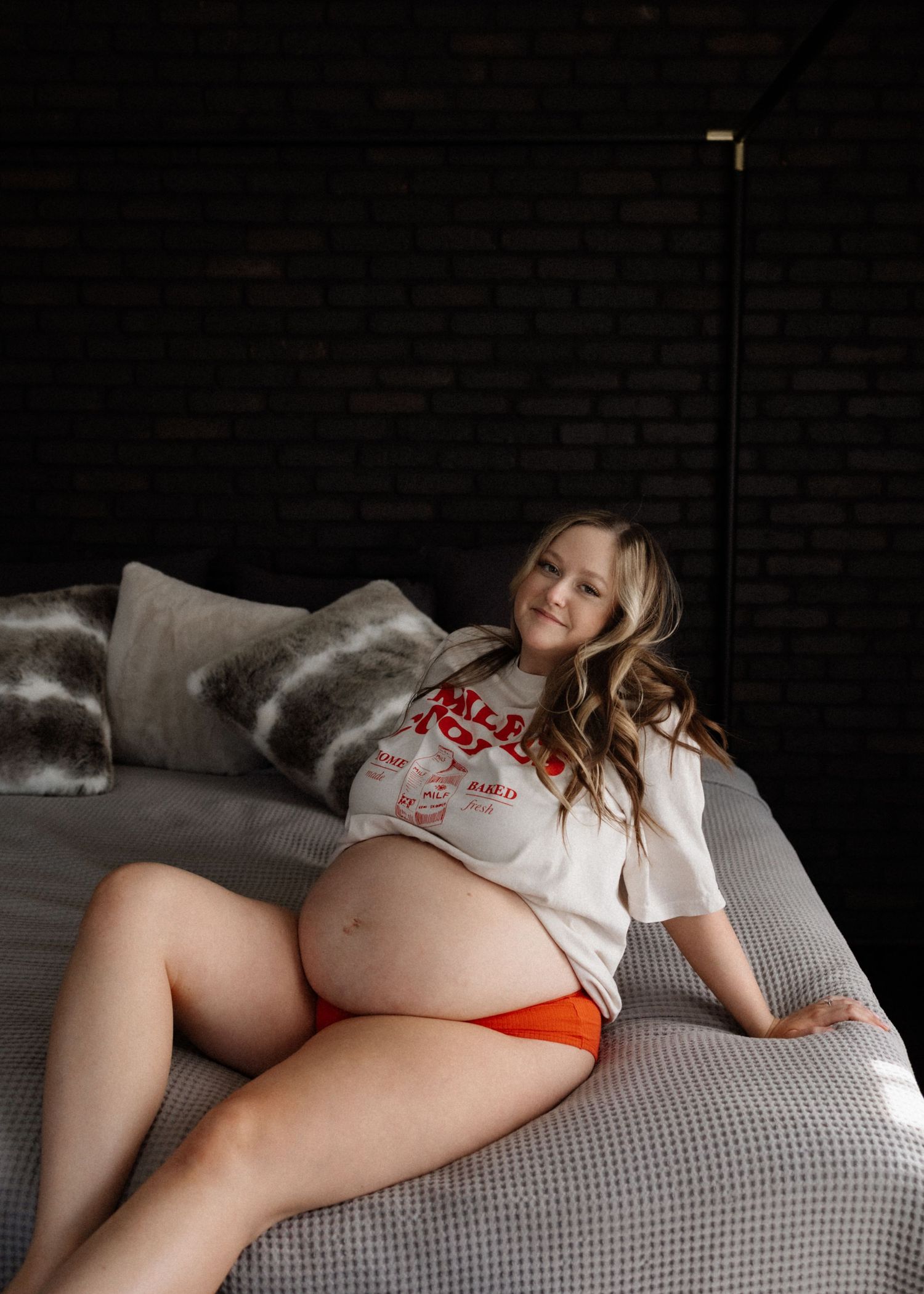 Expectant mother relaxing on a grey couch in casual wear during a maternity photoshoot.