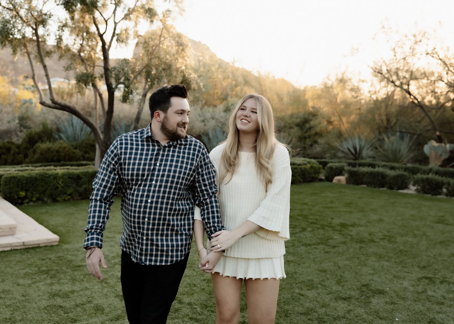 Couple walking hand in hand through landscaped garden at sunset.