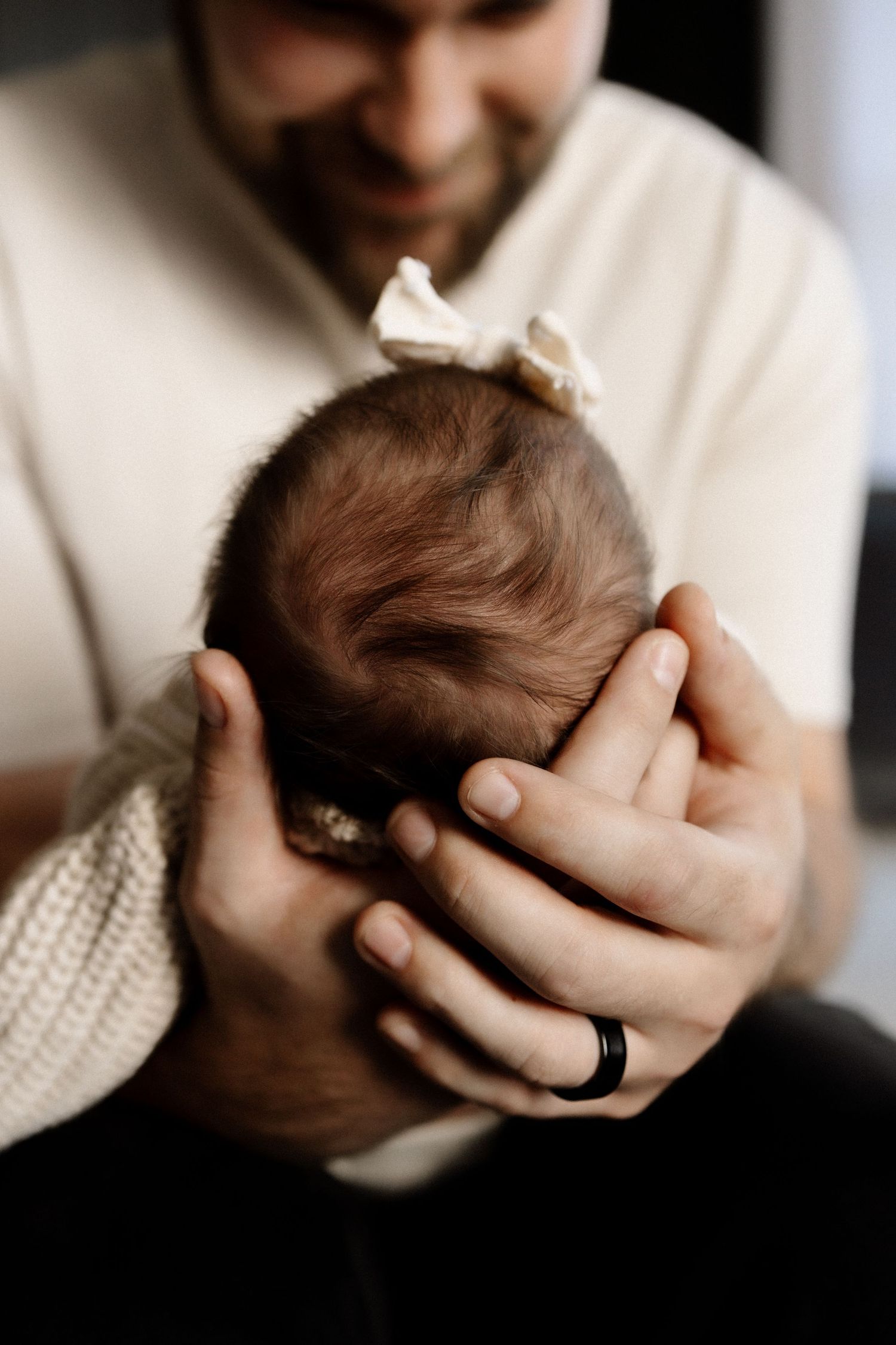 Parent gently holds newborn baby wearing white knit sweater and bow.