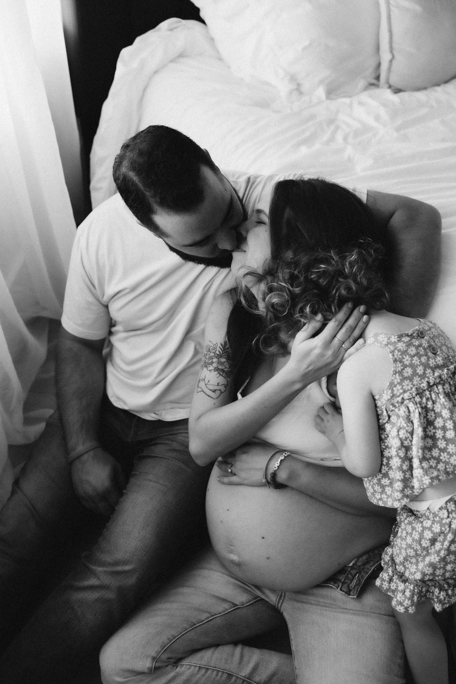 Emotional black and white maternity photo showing intimate family moment on bed.