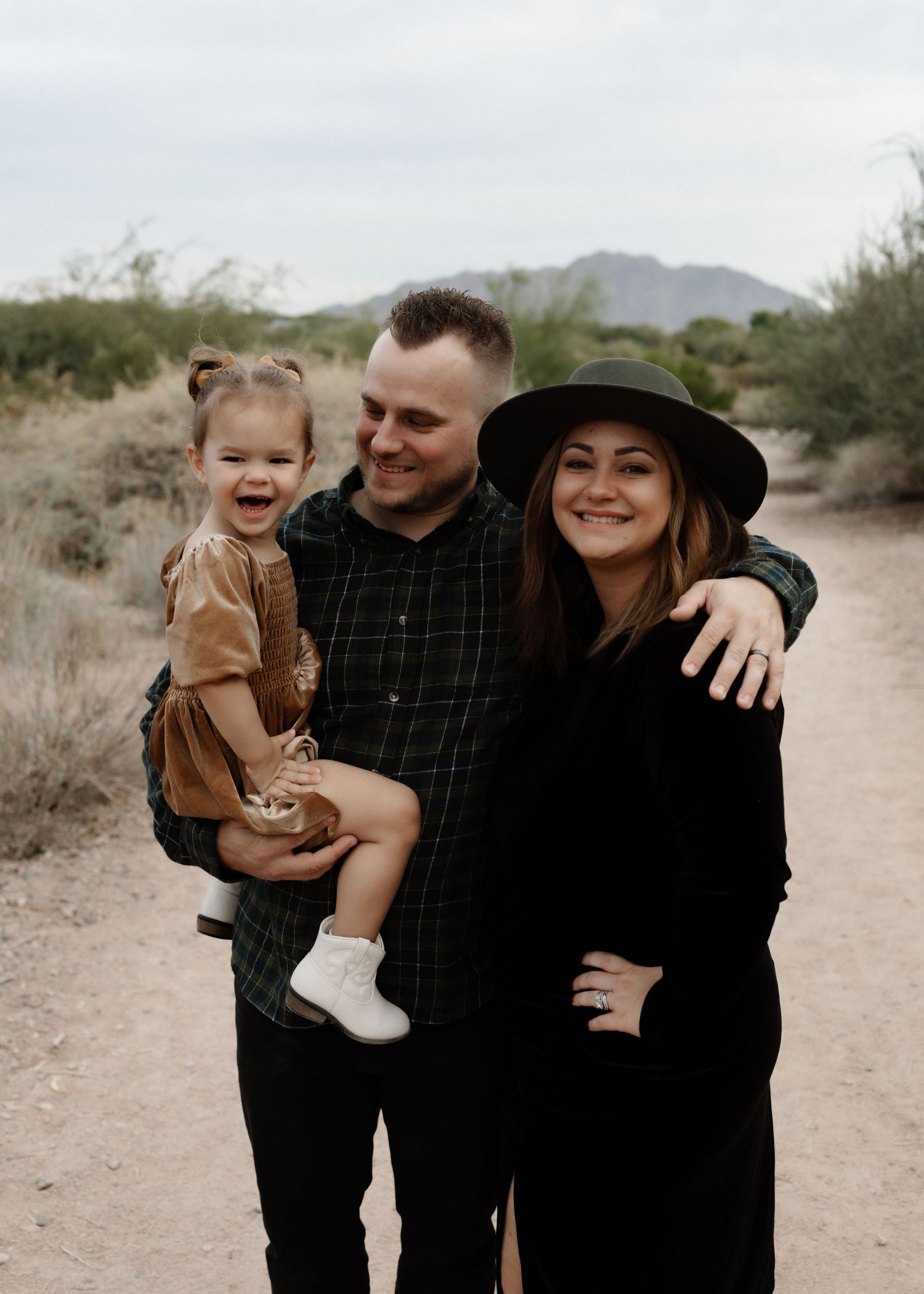 Happy family portrait on desert trail with mountains in background.