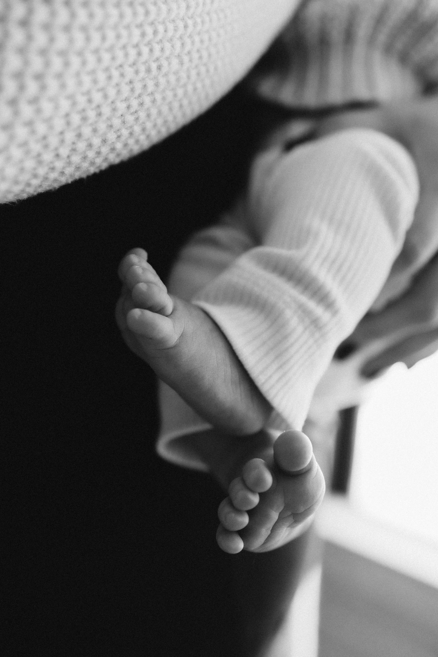 Black and white close-up of tiny baby feet in white knit clothing.