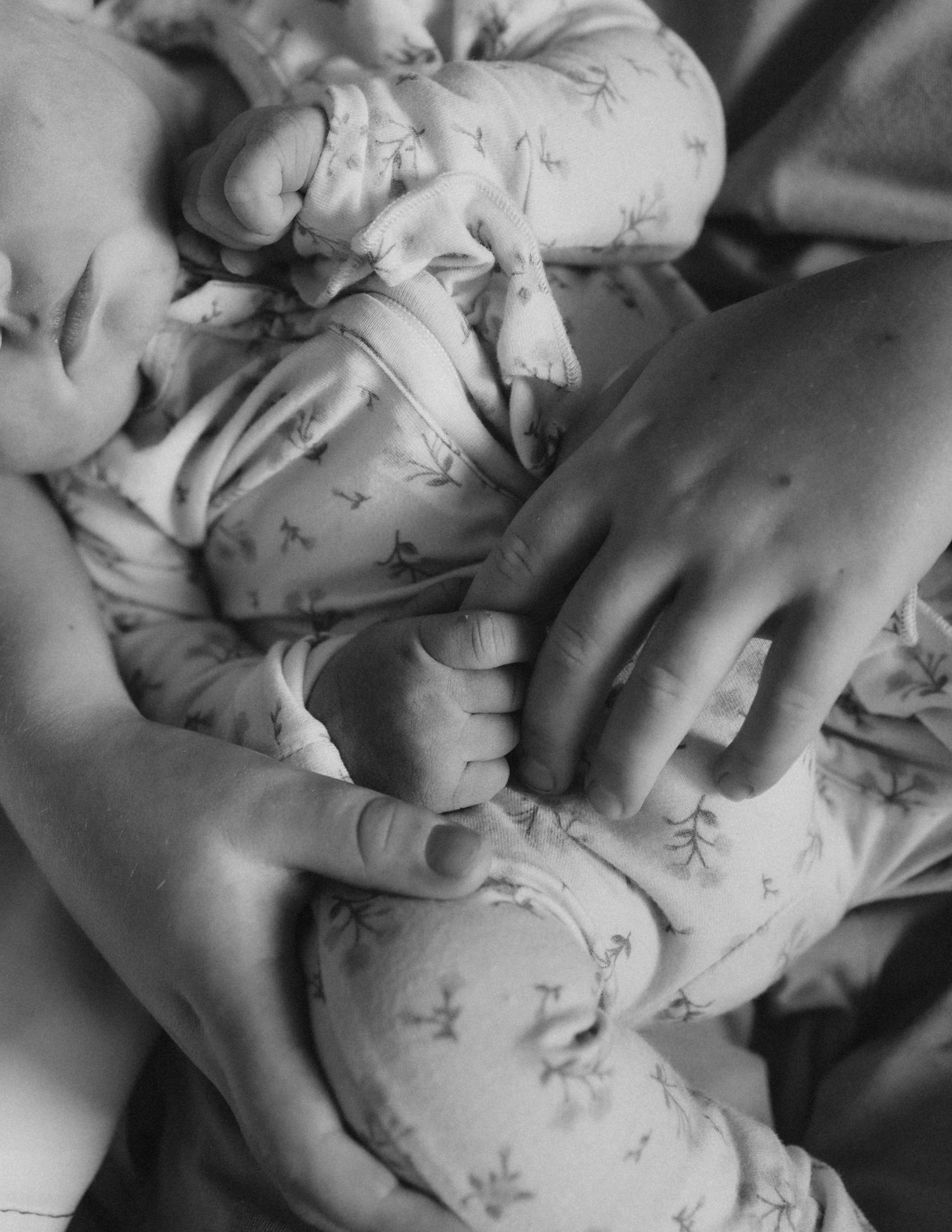 A close-up black and white study of hands gently touching floral patterned fabric, creating an intimate and artistic composition.