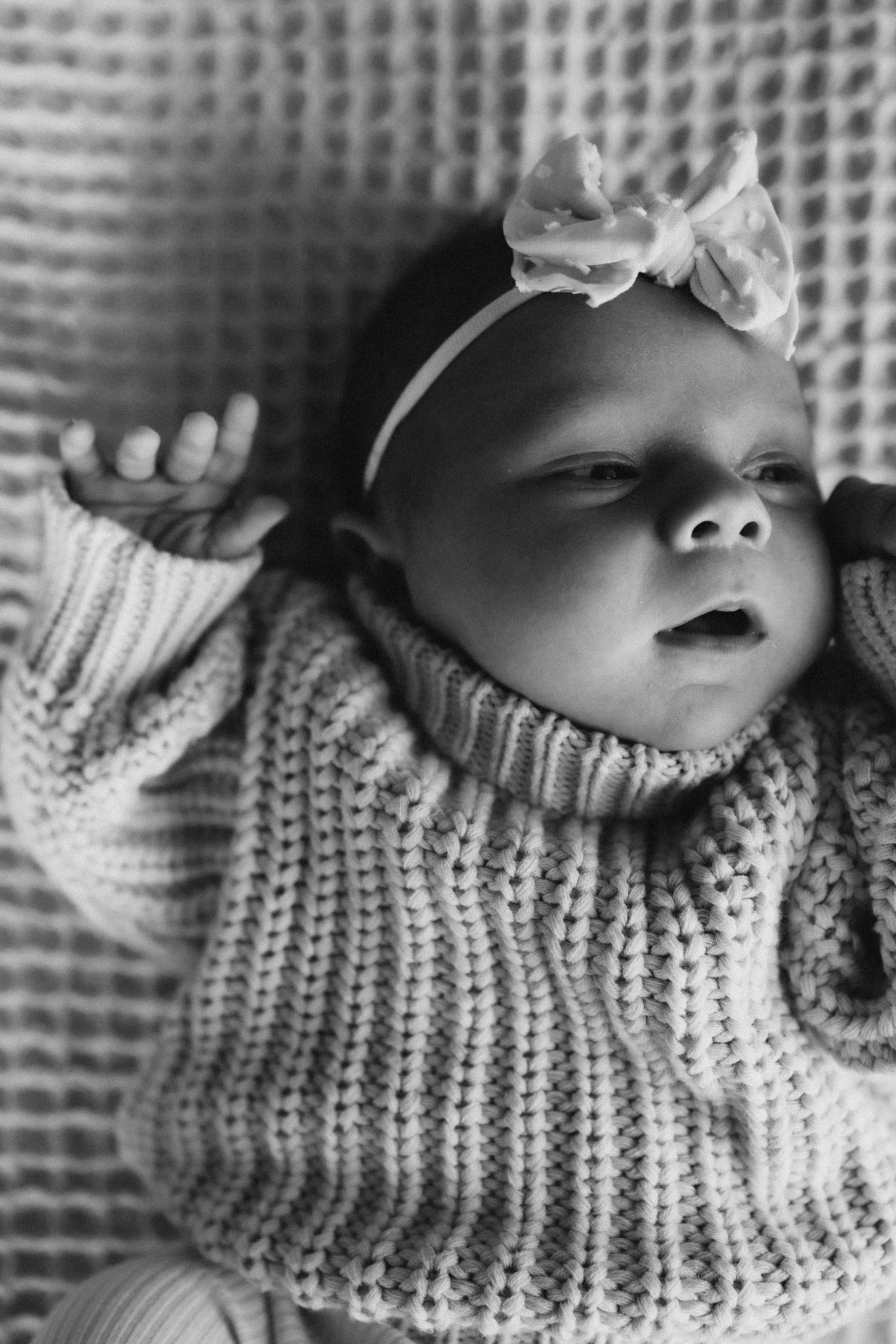 Close-up black and white portrait of sleeping baby wearing knit sweater and bow headband.