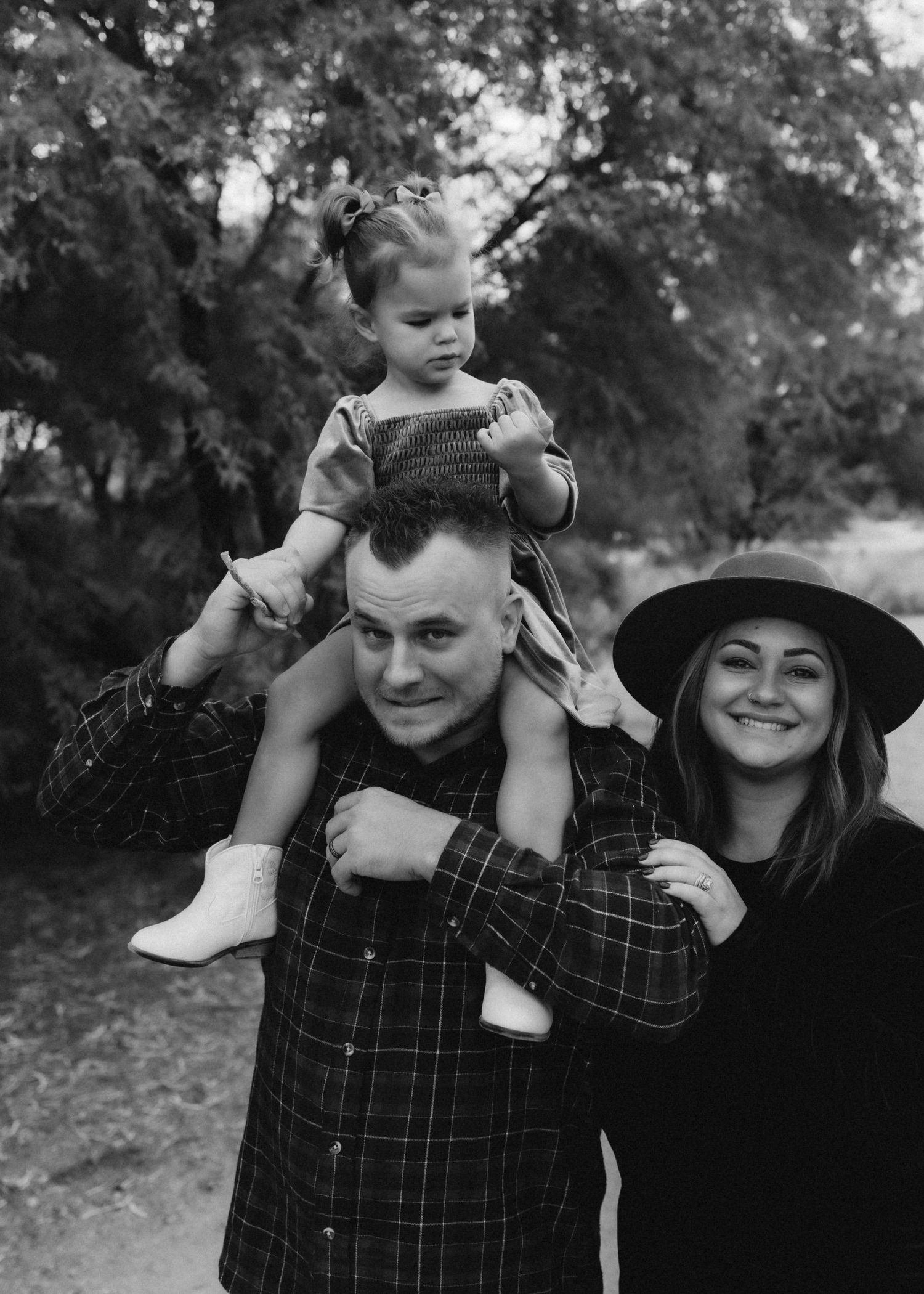 Family photo in black and white showing playful moment outdoors with child on shoulders.