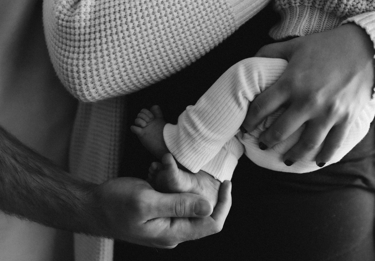 Close-up black and white shot of hands holding a baby bottle during feeding time.
