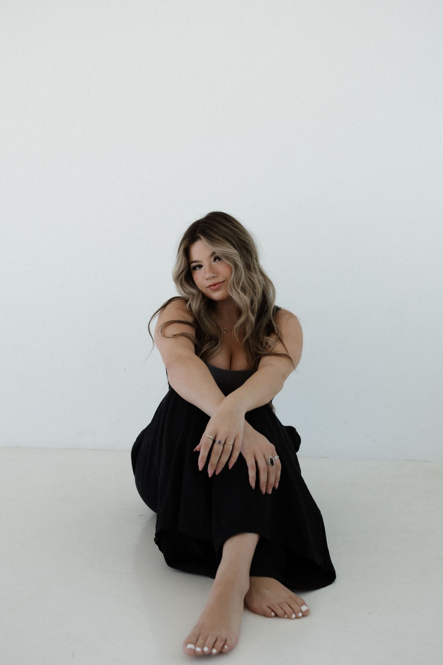 Woman in black dress poses expressively on white background in artistic portrait series.