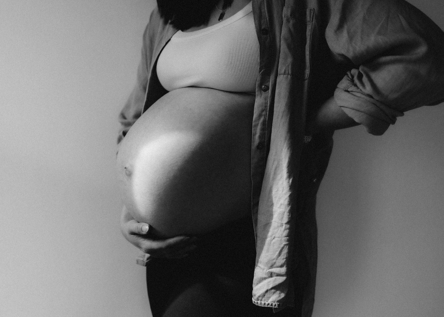Artistic black and white close-up of pregnant belly against minimal background.