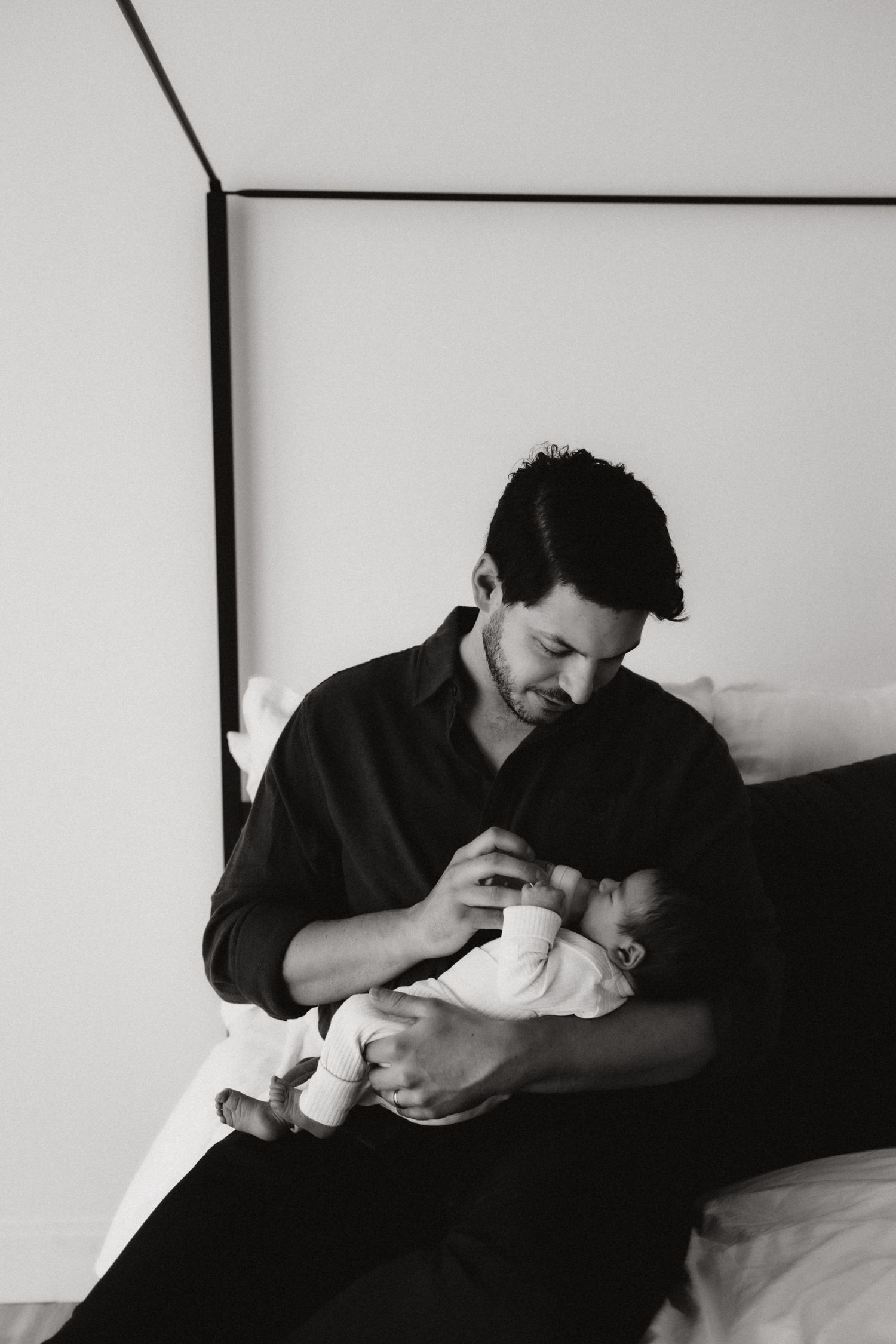 Tender black and white moment of parent feeding newborn on bed.
