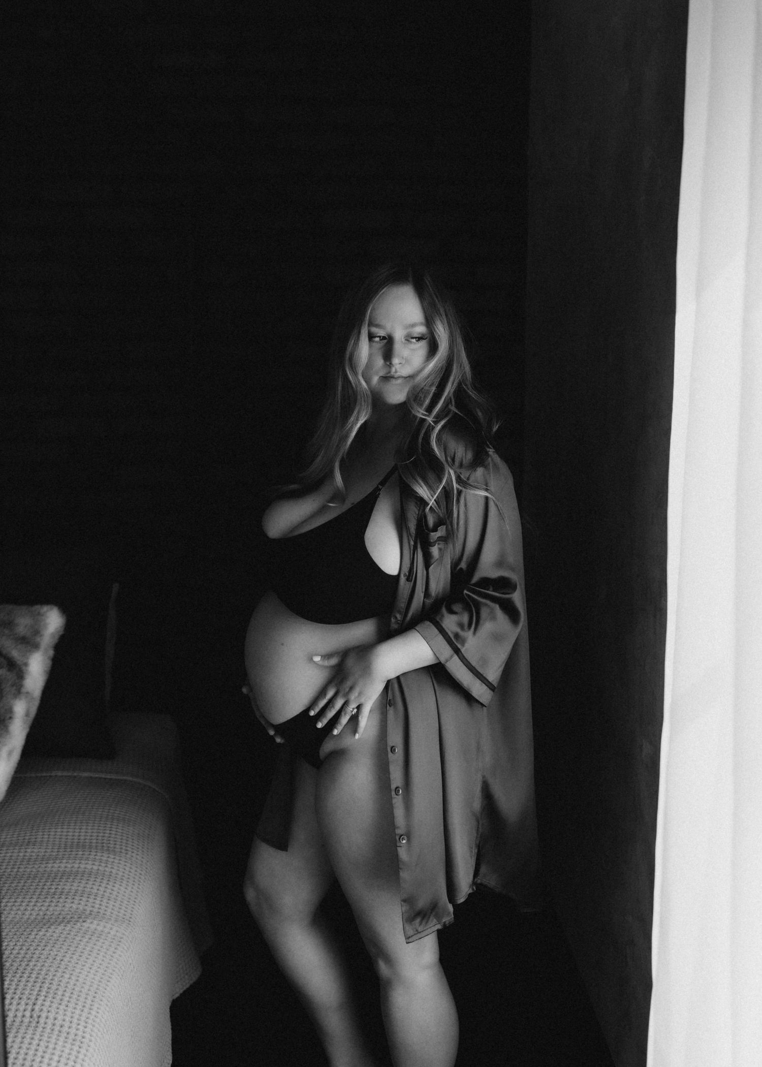 Moody black and white maternity photo with dramatic lighting and flowing robe.